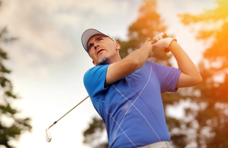 A senior adult man drives a golf ball down the fairway.