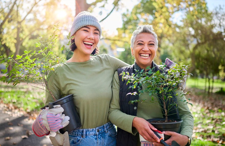 Two woman, one older and the other younger, stand next to each holding plants.