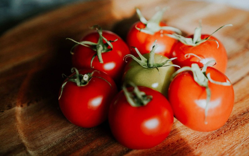 Tomatos on the vine sitting on a wooden cutting board.