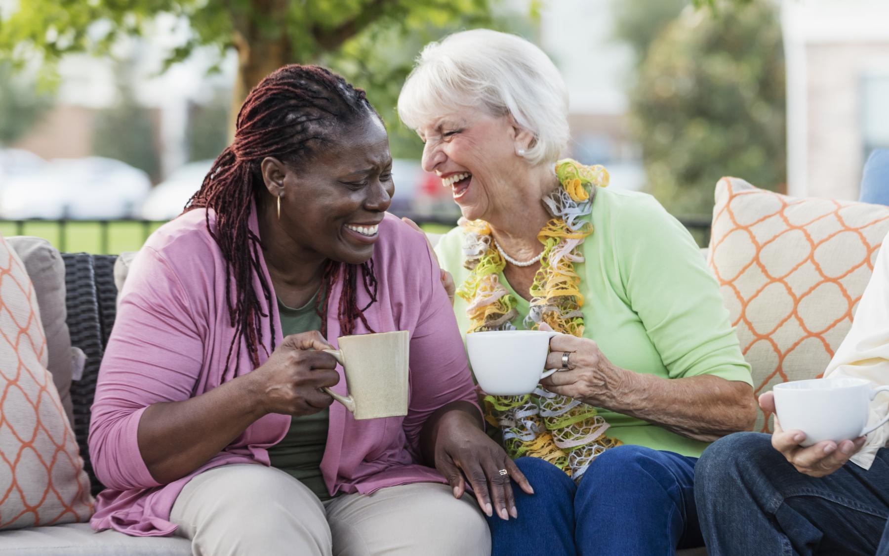 Love where you live two women sitting on a couch outside with mugs laughing