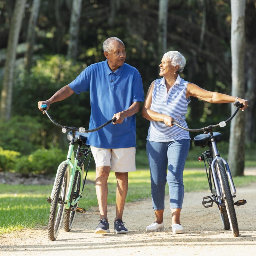 Your Wellness is Our Reason for Being a man and woman walk their bicycles through park