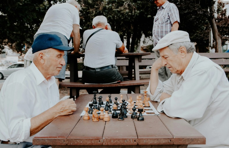 Two senior adult men playing a game of chess in the park.