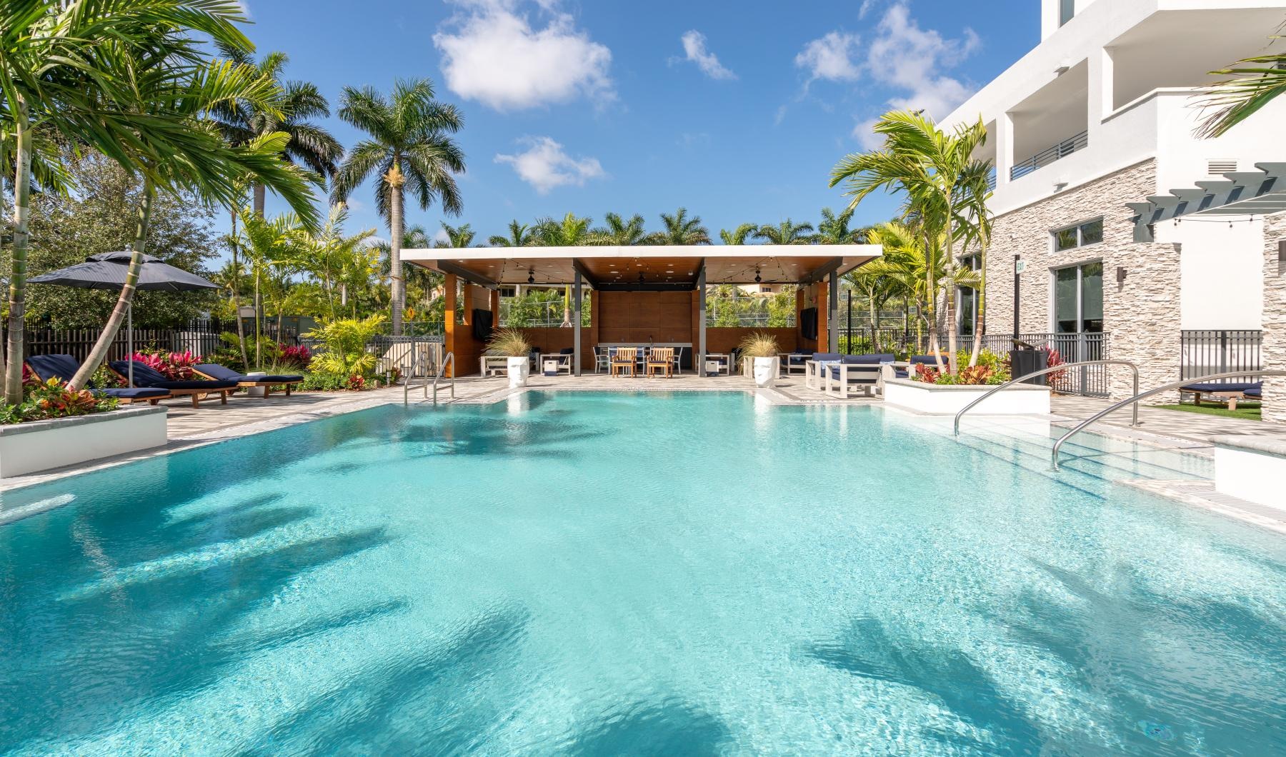 Large sparkling blue pool with a large deck and lounge chairs 